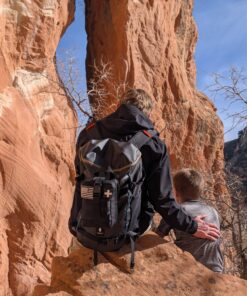 Hiker climbing on red rock with Med Kit Pro first aid kit attached to backpack using MOLLE webbing